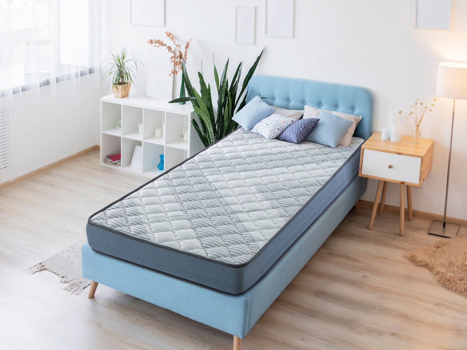 Una cama azul con colchón y almohadas se encuentra en un dormitorio junto a una mesita de noche.