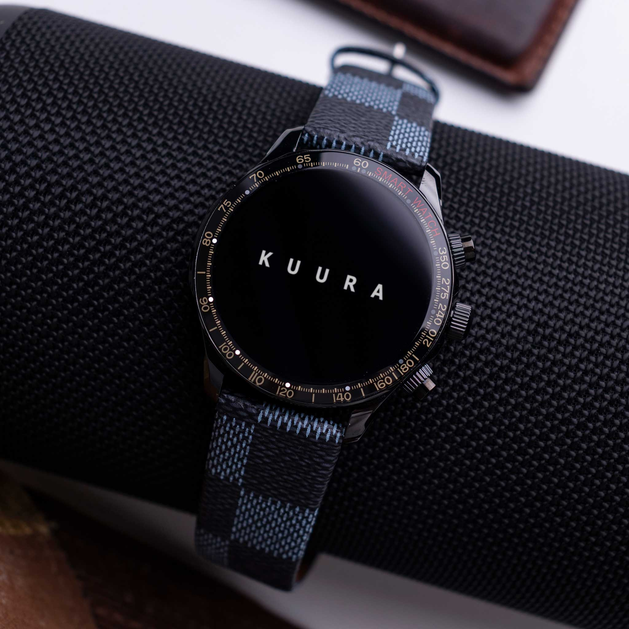 Czarny smartwatch w kratkę leży na czarnej fakturze siatki.