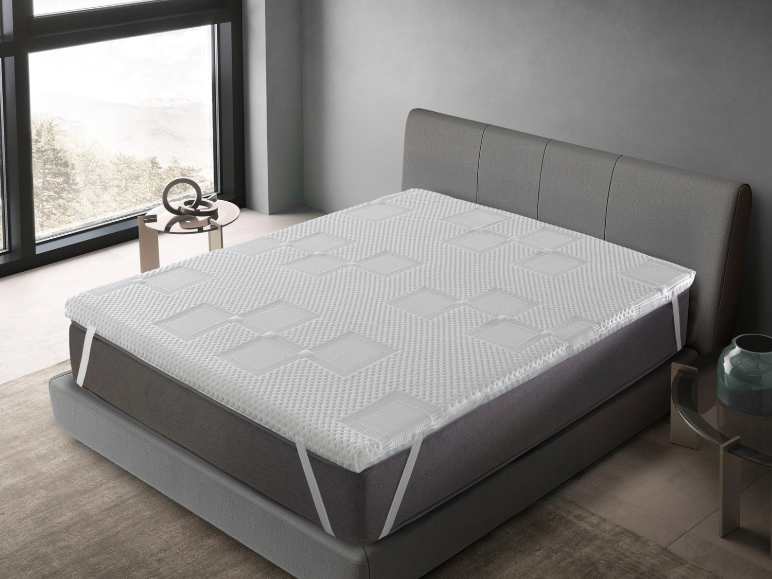 Un cubrecolchón blanco con patrón de diamantes sobre una cama gris con cabecero.