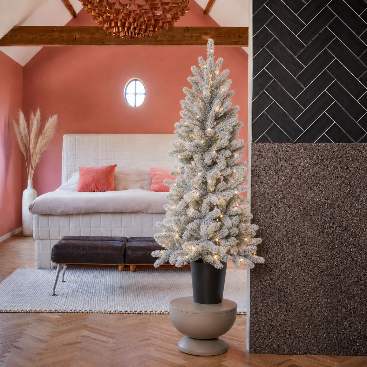 Ein weißer Weihnachtsbaum mit Lichtern steht neben einem Bett mit Lachsfarbenen Kissen.