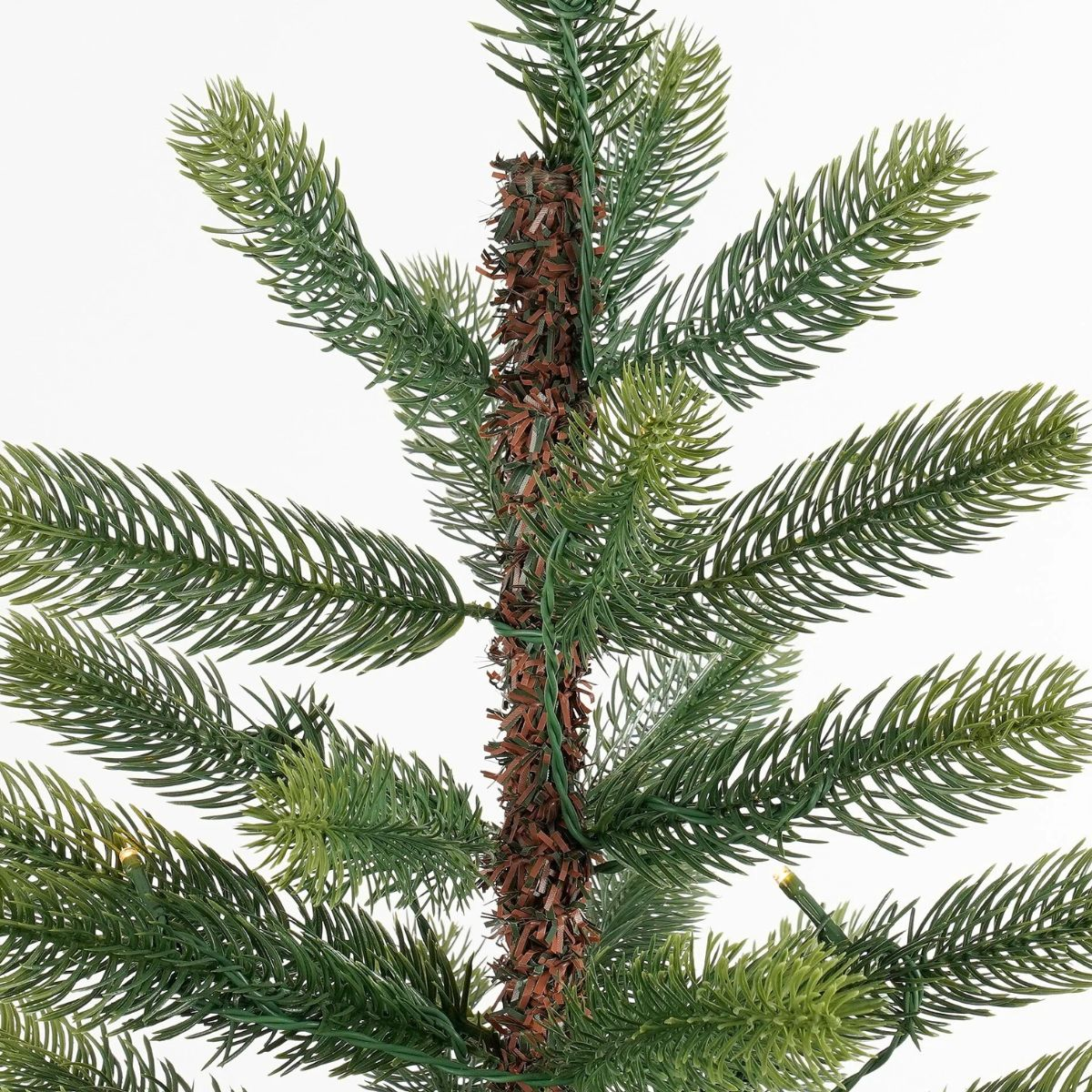Close-up of an artificial Christmas tree with green needles and a brown trunk.