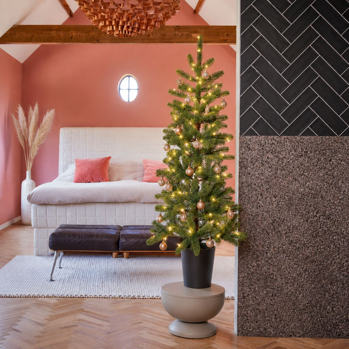 A decorated Christmas tree stands beside a bed in a pink room with wooden floors.