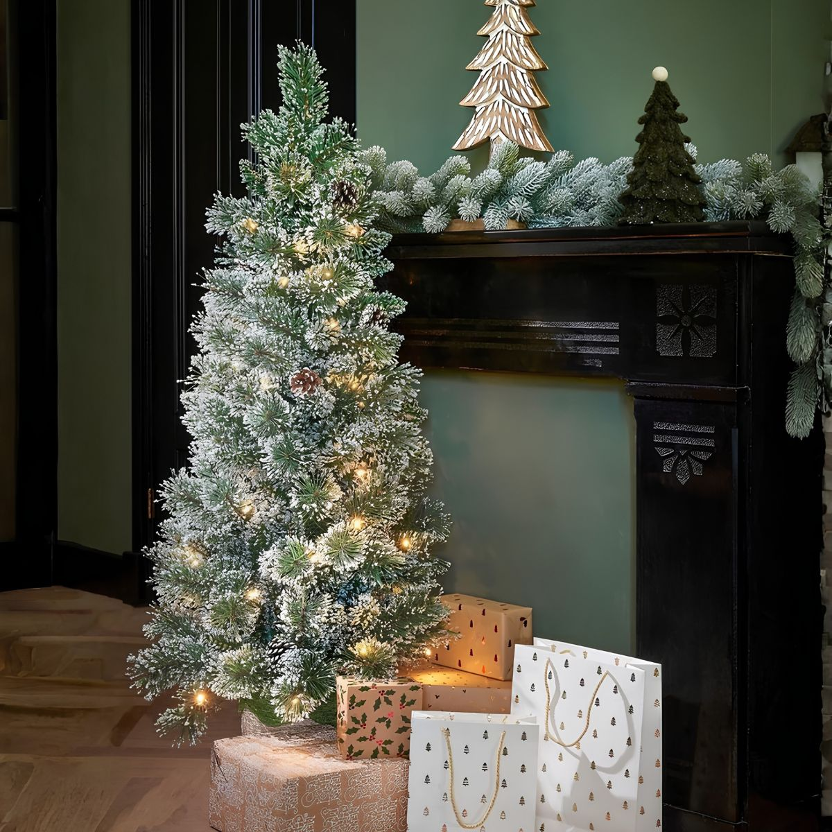 A frosted Christmas tree with lights sits beside a fireplace with gifts.
