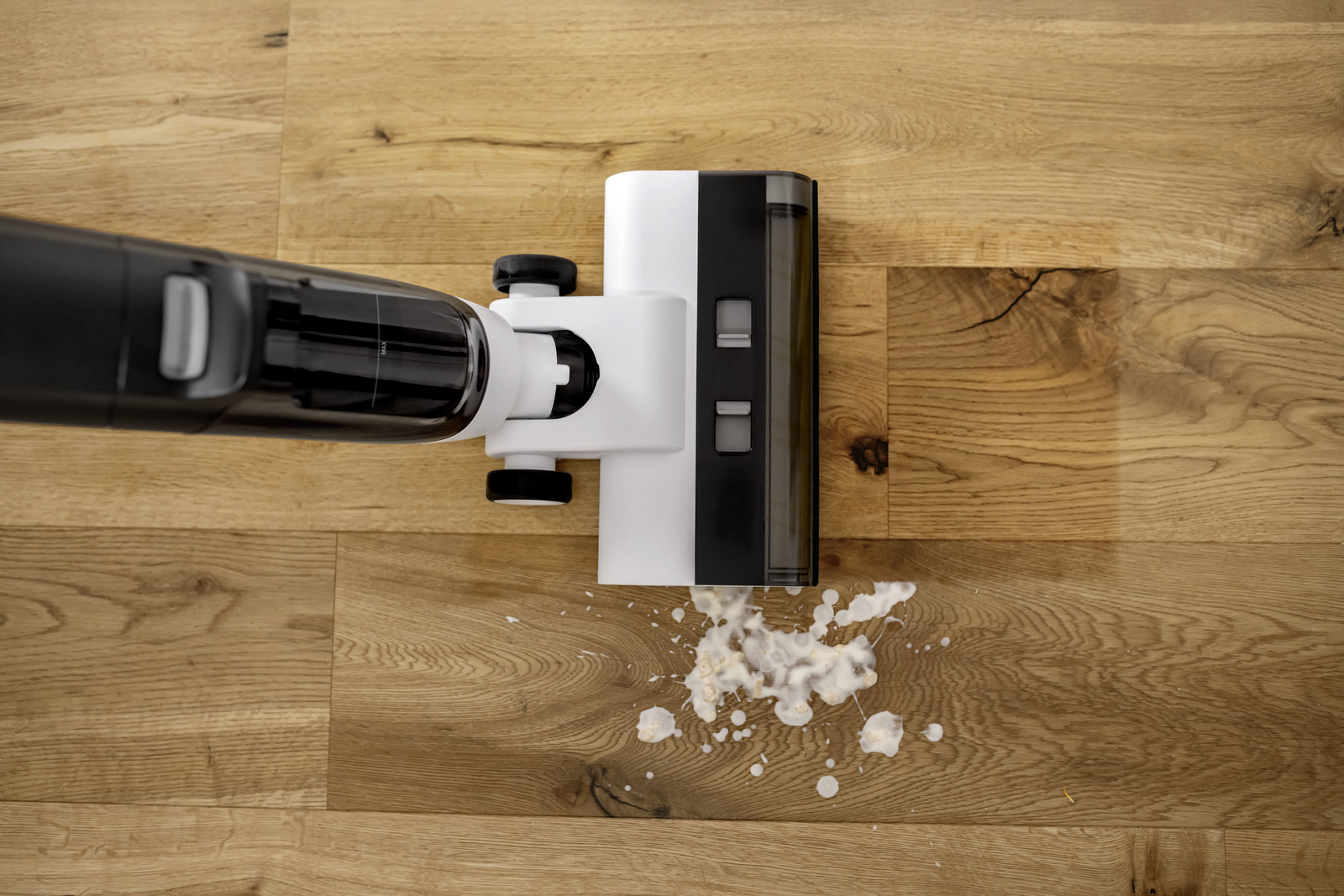 Un aspirapolvere bianco per liquidi e solidi pulisce una macchia su un pavimento in legno.