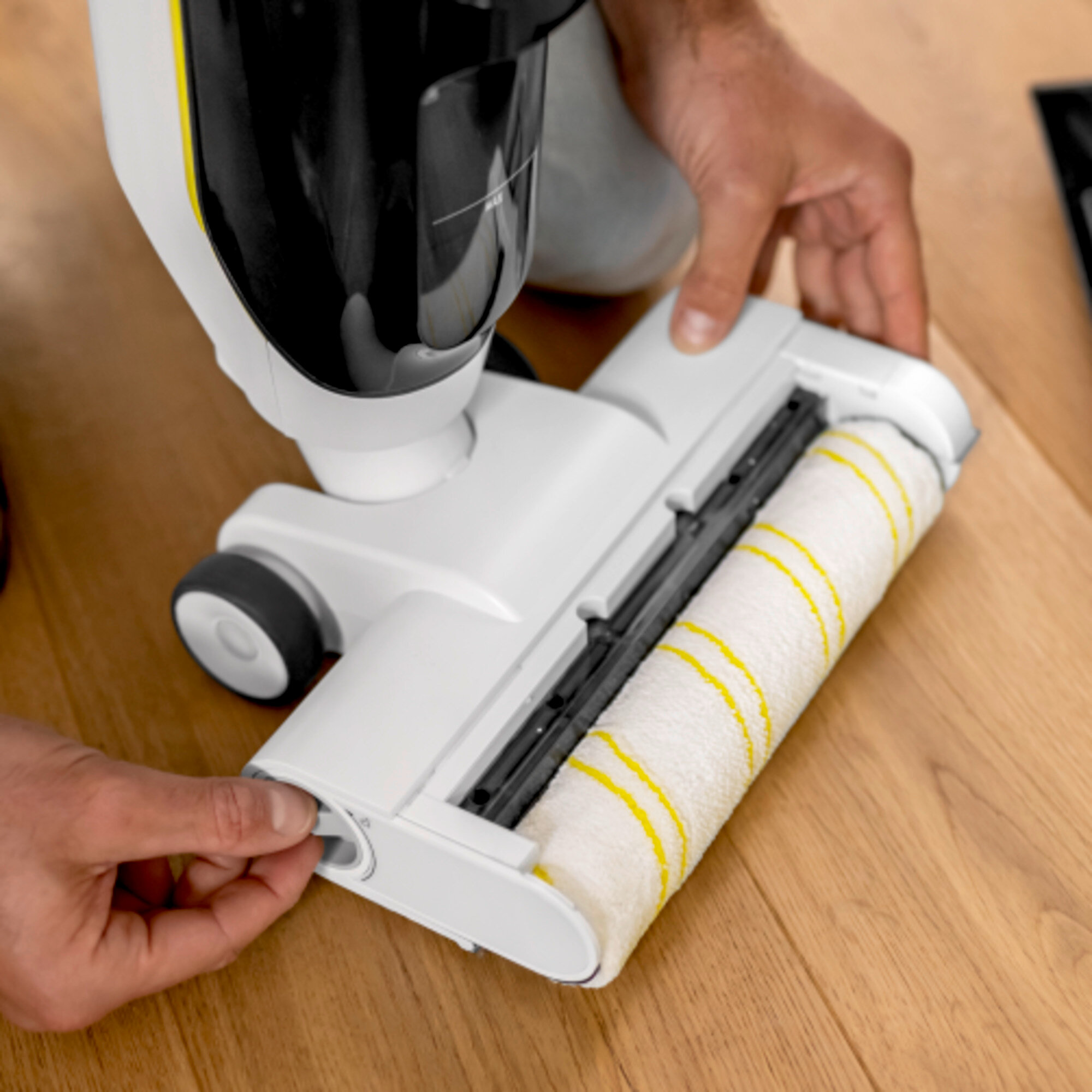 Mani che montano il rullo spazzola su aspirapolvere bianco su parquet.