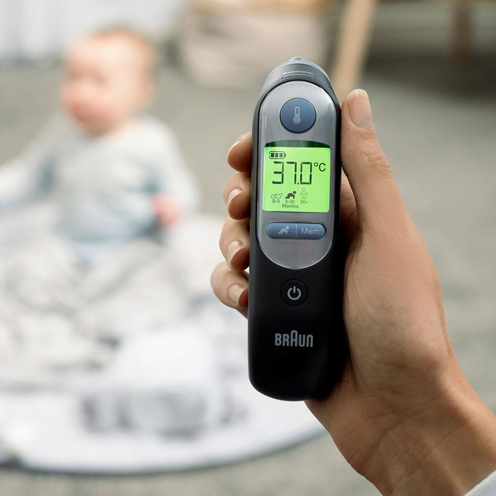 Una mano tiene un termometro digitale che mostra 37,0°C davanti a un bambino sfocato.