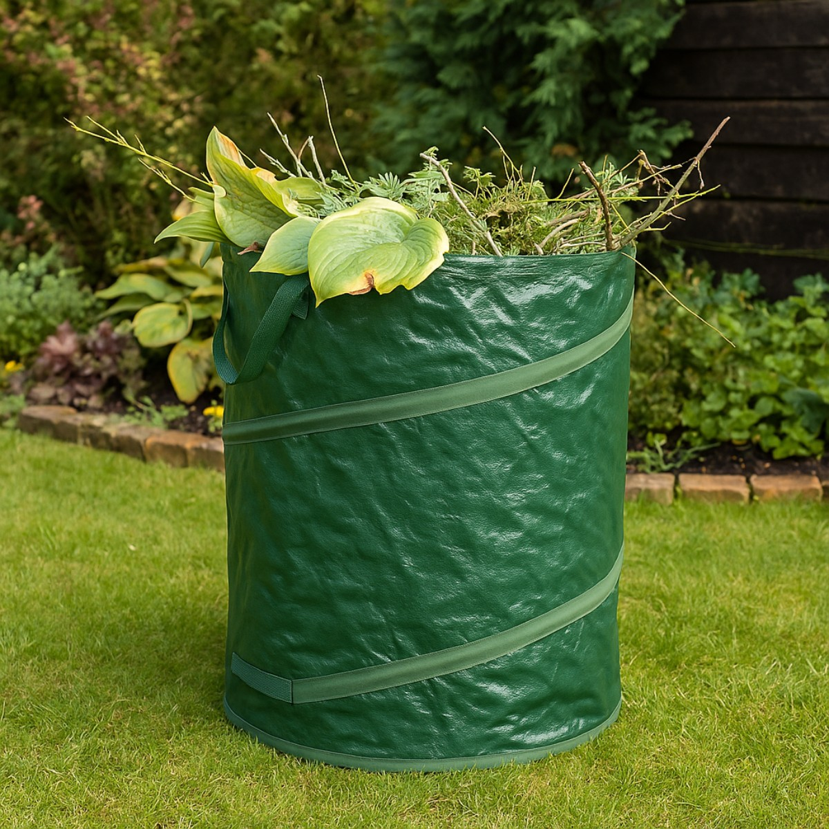 Un sac à déchets de jardin vert rempli de feuilles et de branches est sur l'herbe.