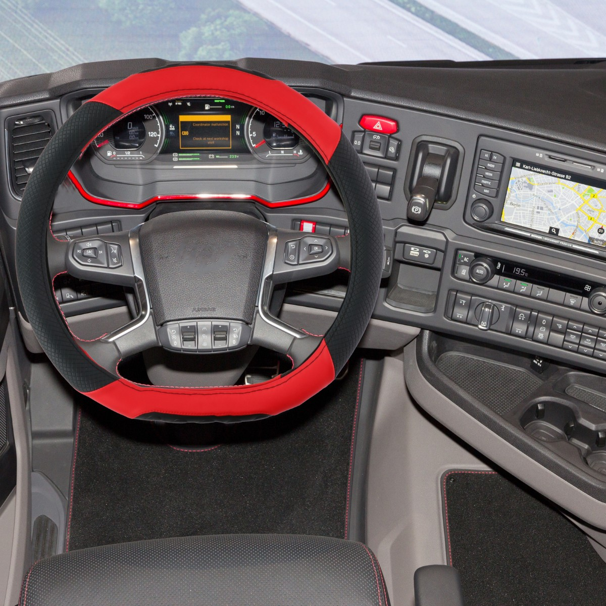 Red and black steering wheel cover in a truck cab. Dashboard displays are visible.