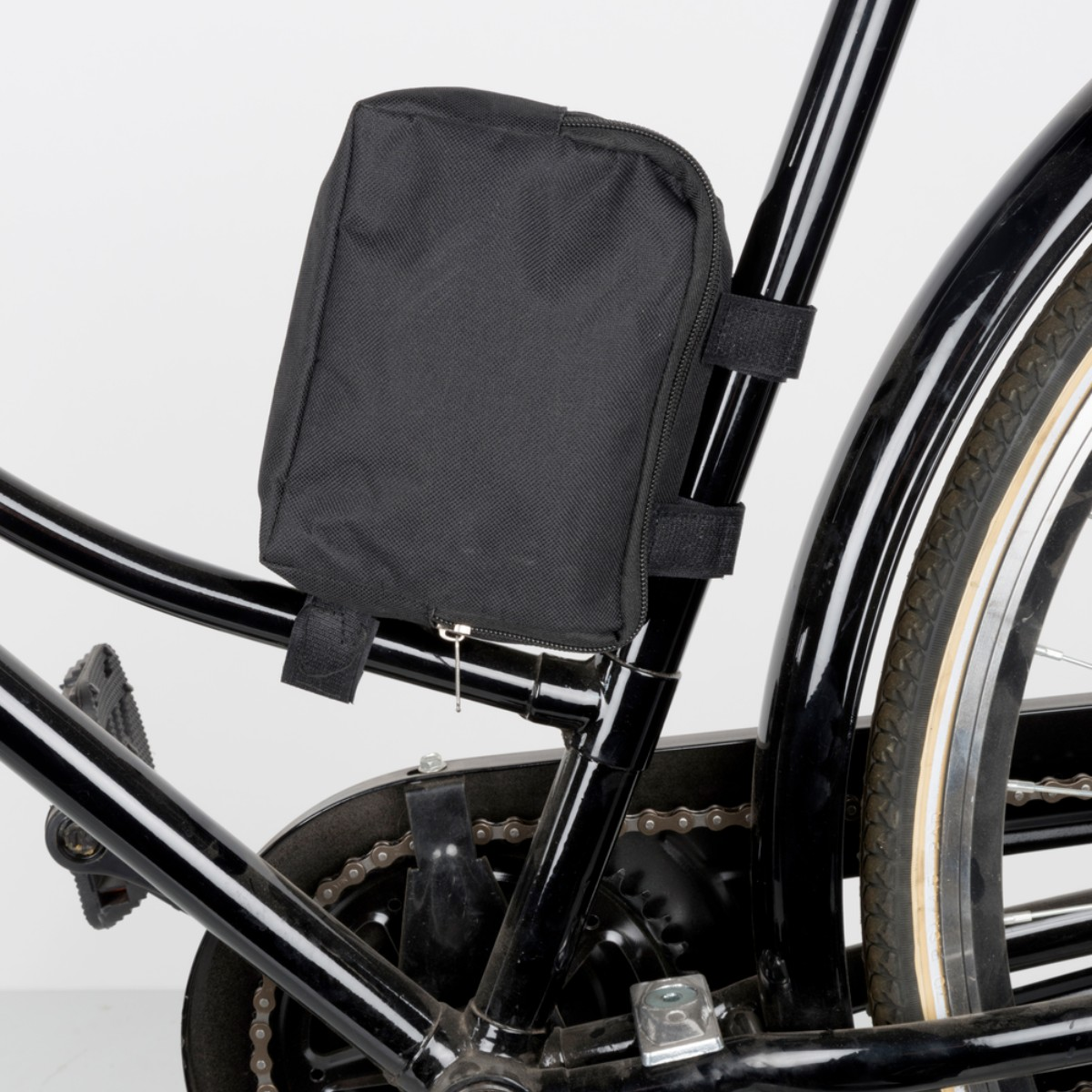 Schwarze Fahrradtasche am Rahmen befestigt, mit Kette und Rad im Hintergrund.