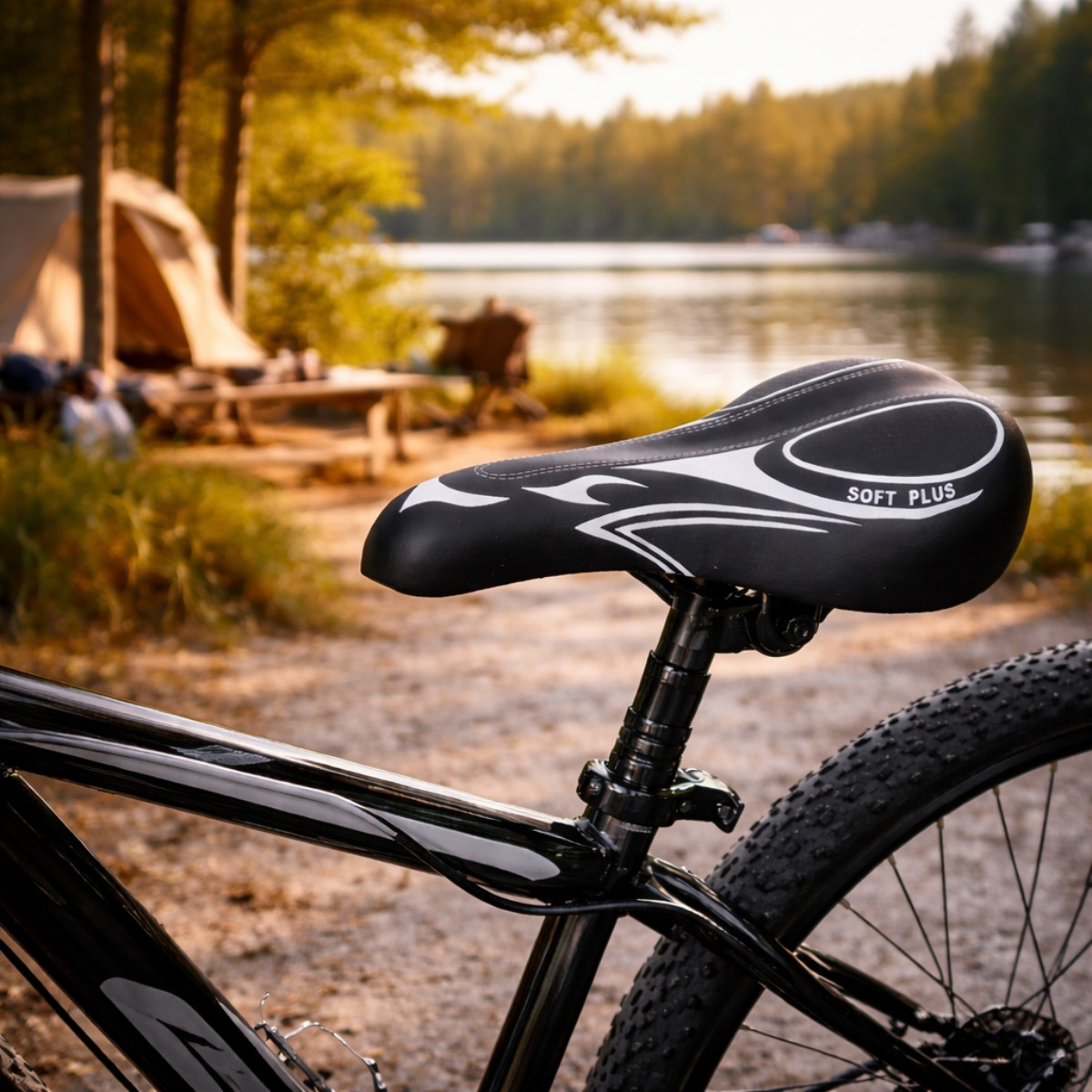 Close-up van een zwart fietszadel met wit design, camping en meer op de achtergrond.
