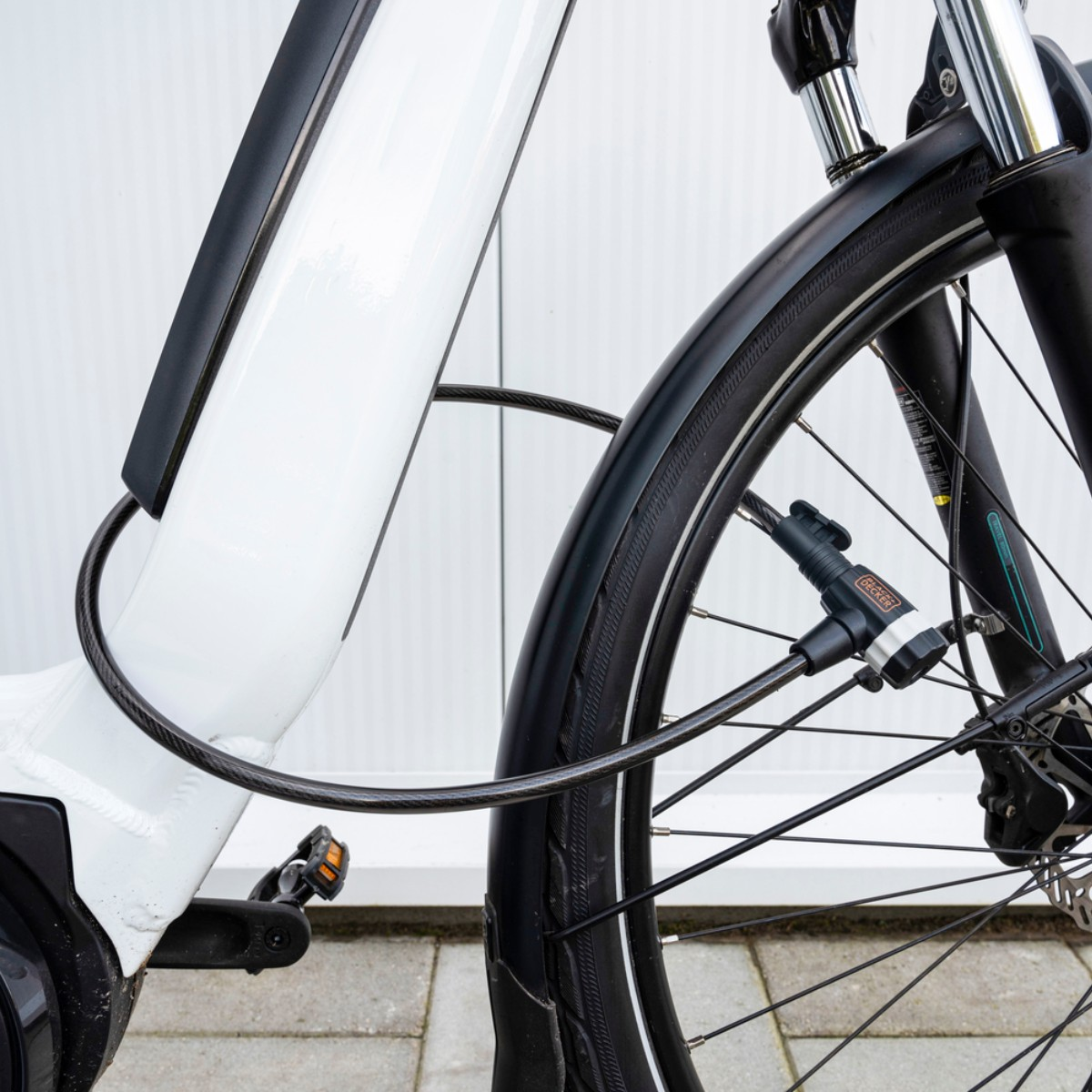 A white bicycle with a black cable lock threaded through the frame and wheel.