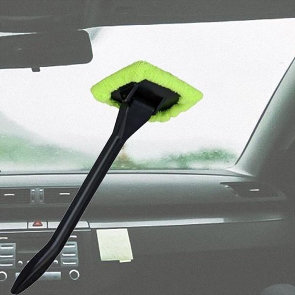 Strumento di pulizia con testa verde e manico nero su cruscotto auto.