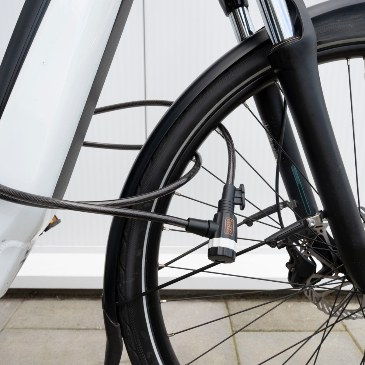 A black cable lock secures a white bicycle's front wheel and frame.