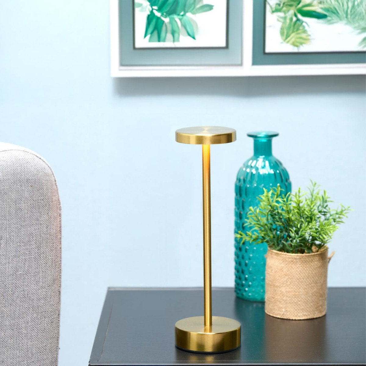 Goldene Lampe auf einem Tisch neben einer blauen Vase und einer Pflanze.