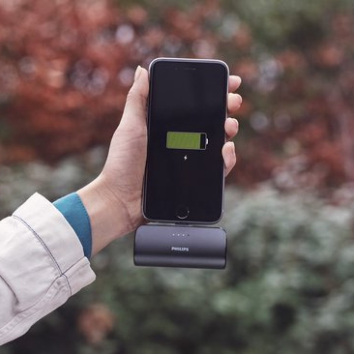 Une main tient un smartphone en charge sans fil sur une batterie externe Philips.