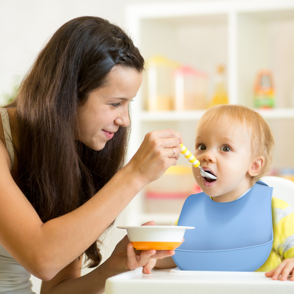 Een vrouw voedt een baby met een lepel, baby draagt een blauw slabbetje.
