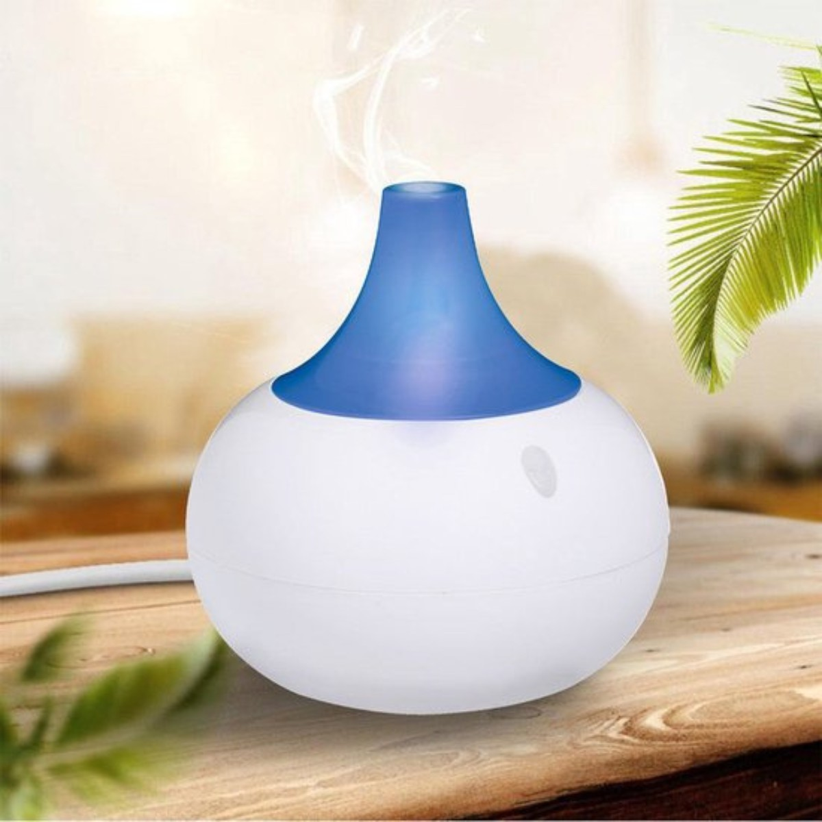 Weißer Diffusor mit blauem Oberteil, der Dampf auf einem Holztisch abgibt.