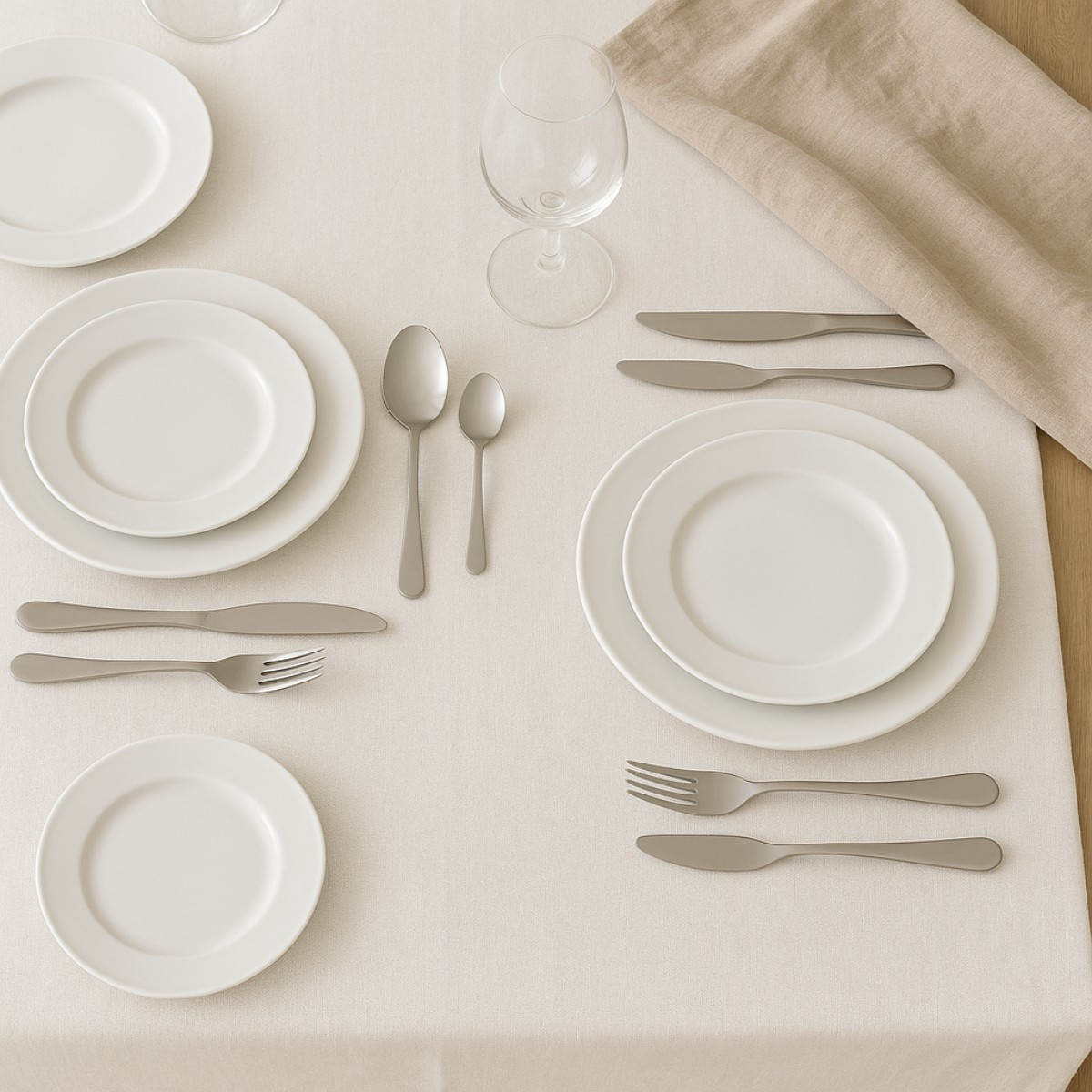 Ein gedeckter Tisch mit weißen Tellern, Besteck, Löffeln und einem Weinglas.