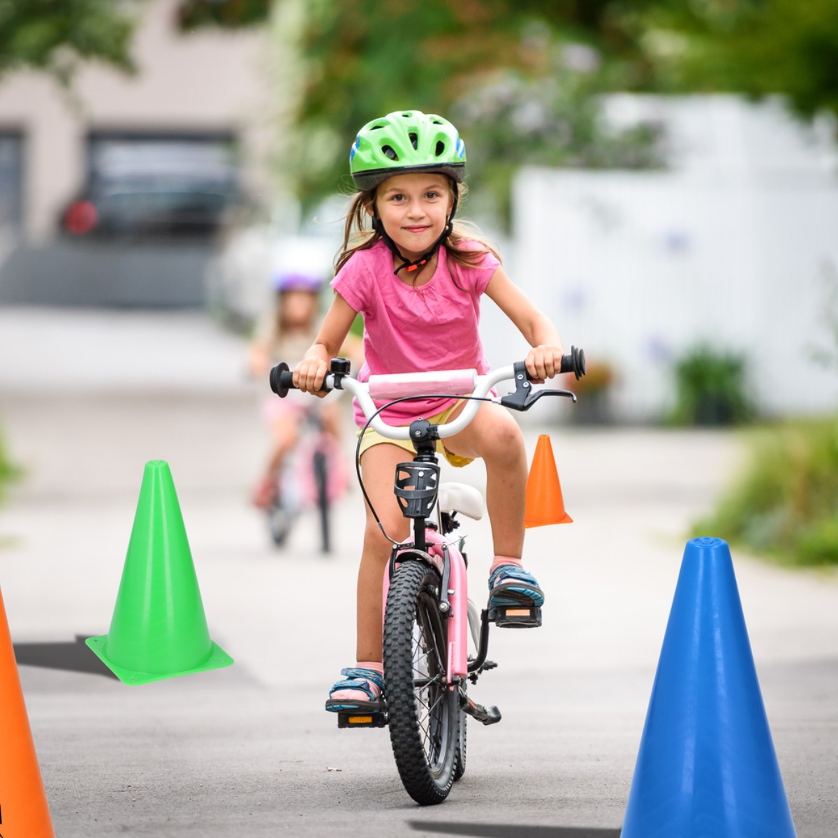 Una bambina con casco verde va in bicicletta, circondata da coni colorati.