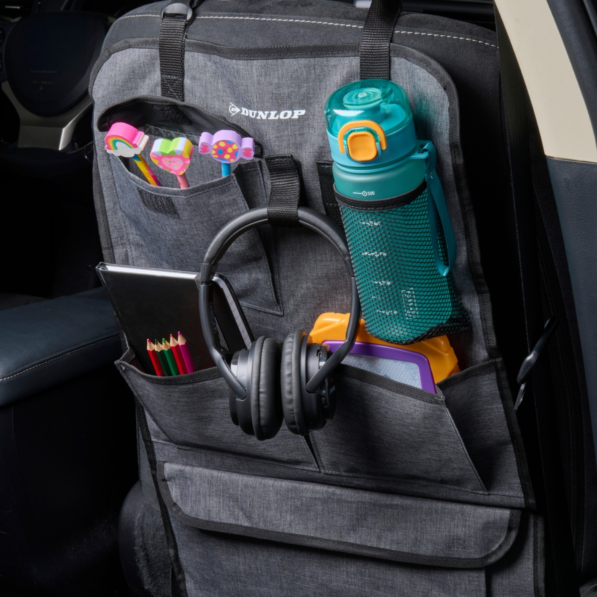 Autostoel organizer met kleurrijke gummen, potloden, koptelefoon, tablet en waterfles.