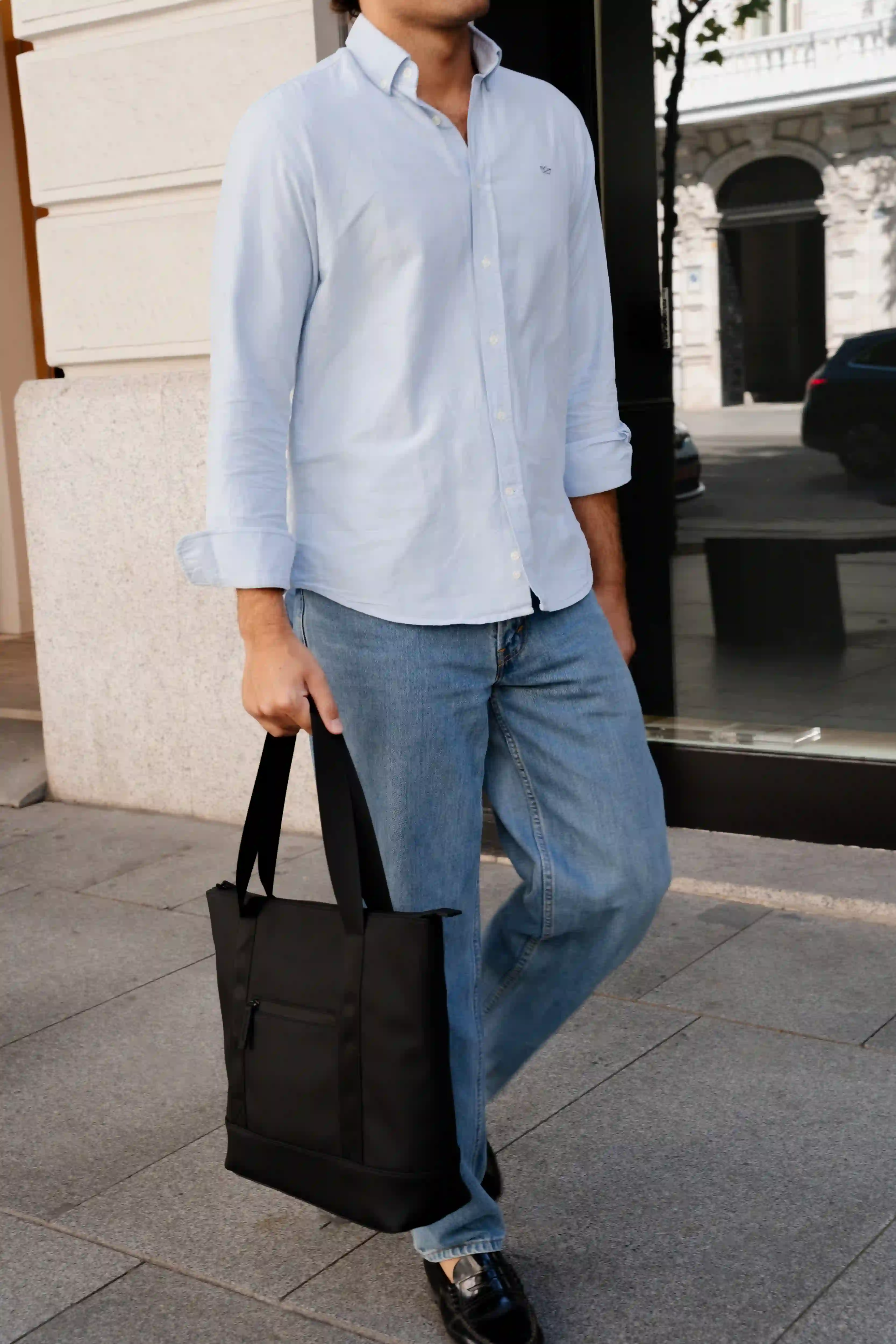 Uomo in camicia azzurra e jeans porta una borsa nera.