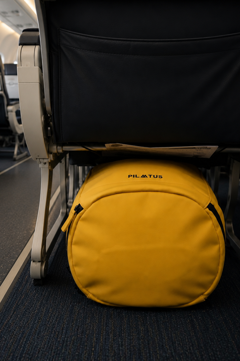 Borsone giallo con logo Pilatus sotto i sedili dell'aereo su tappeto blu.