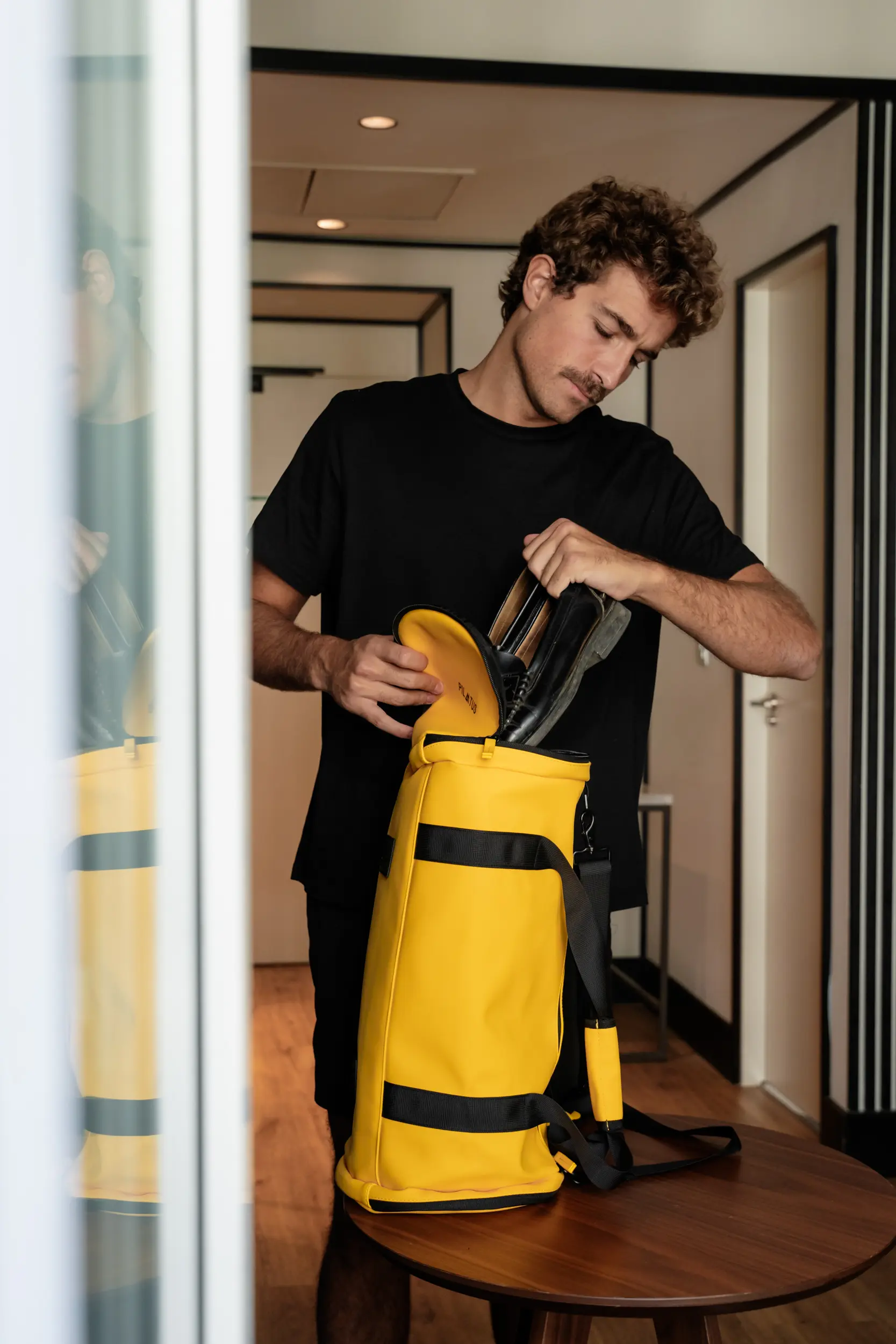 Uomo in maglietta nera mette scarpe nere in una borsa gialla.