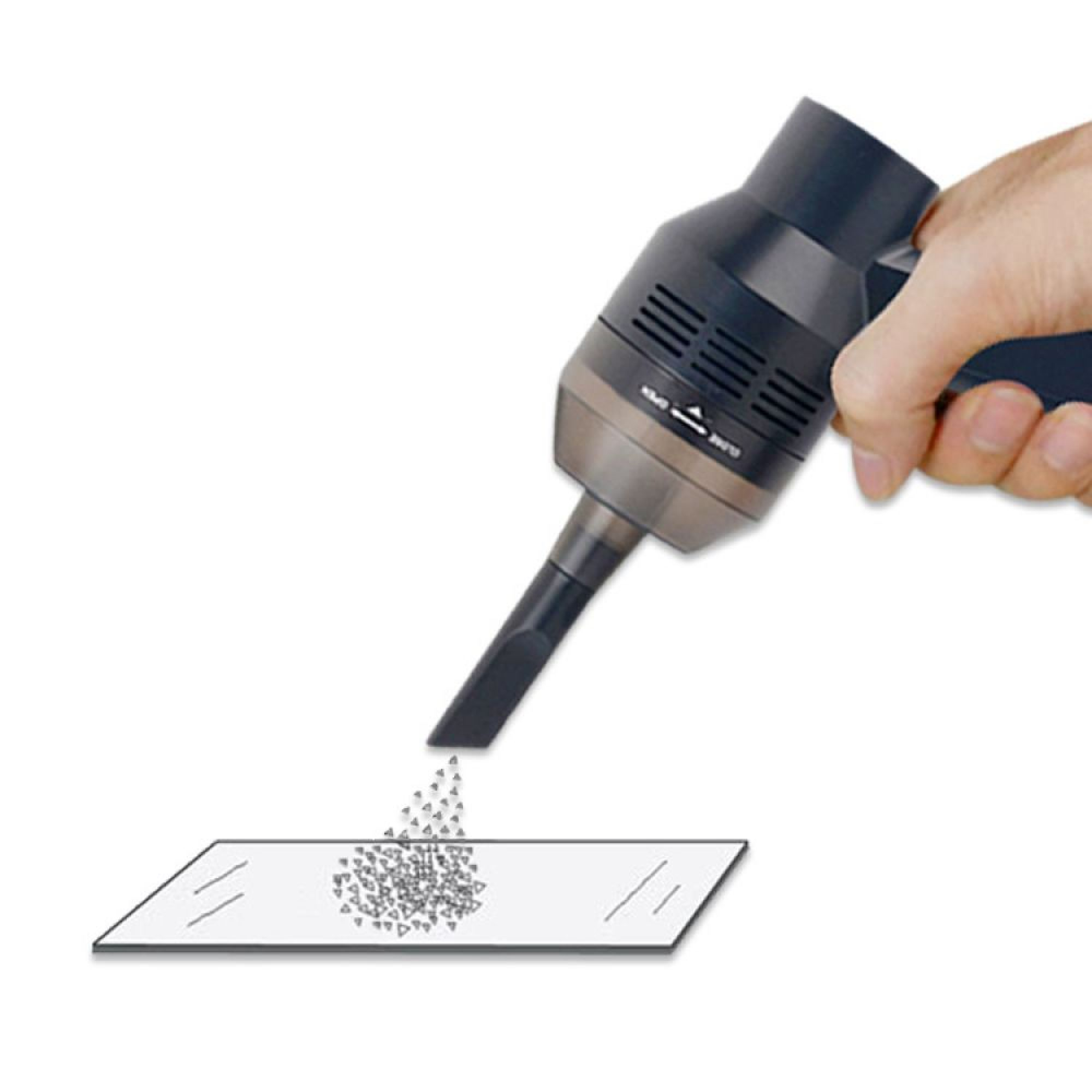 Eine Hand hält einen schwarzen Mini-Staubsauger, der kleine graue Partikel von einer weißen rechteckigen Oberfläche aufsaugt.