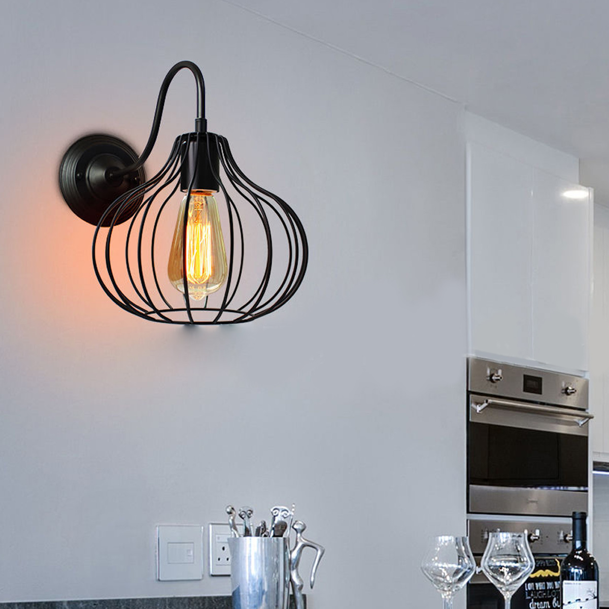 Eine schwarze industrielle Wandleuchte mit Drahtkäfig und Edison-Birne hängt an einer weißen Wand.