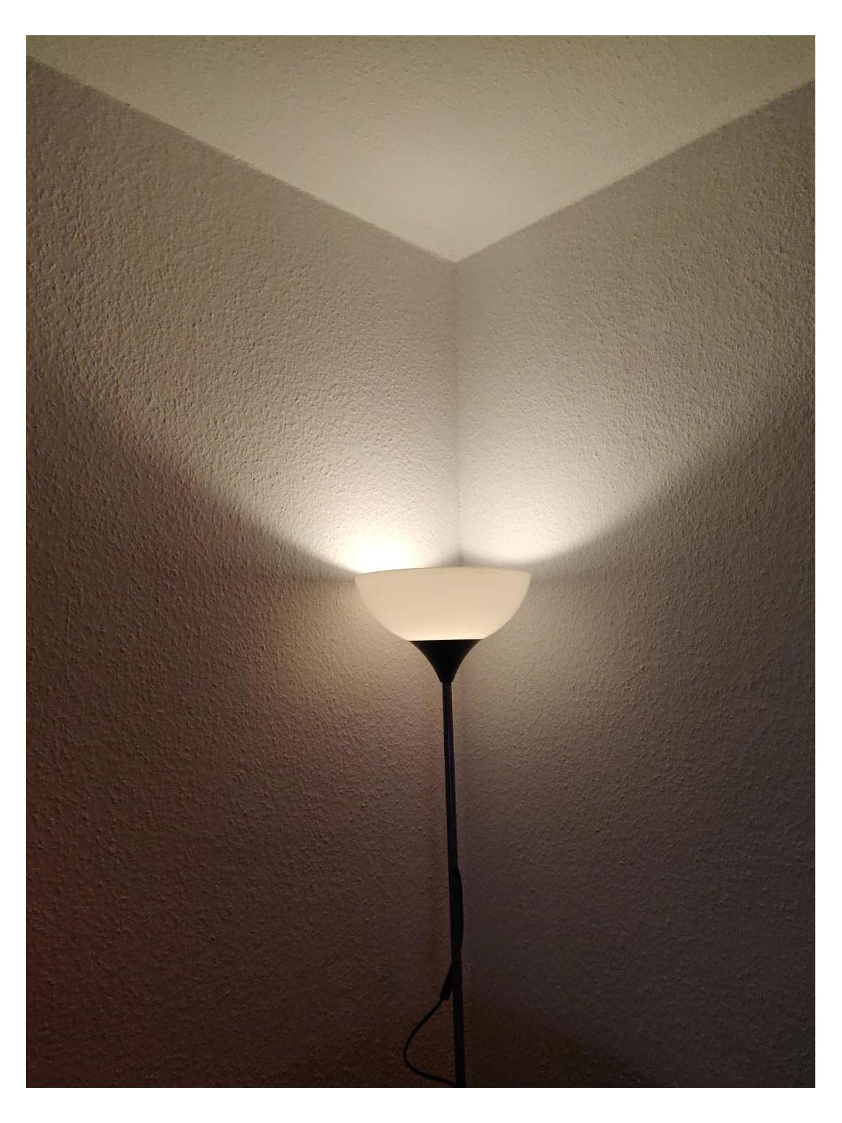 Eine Stehlampe beleuchtet eine weiße Ecke mit Schatten.