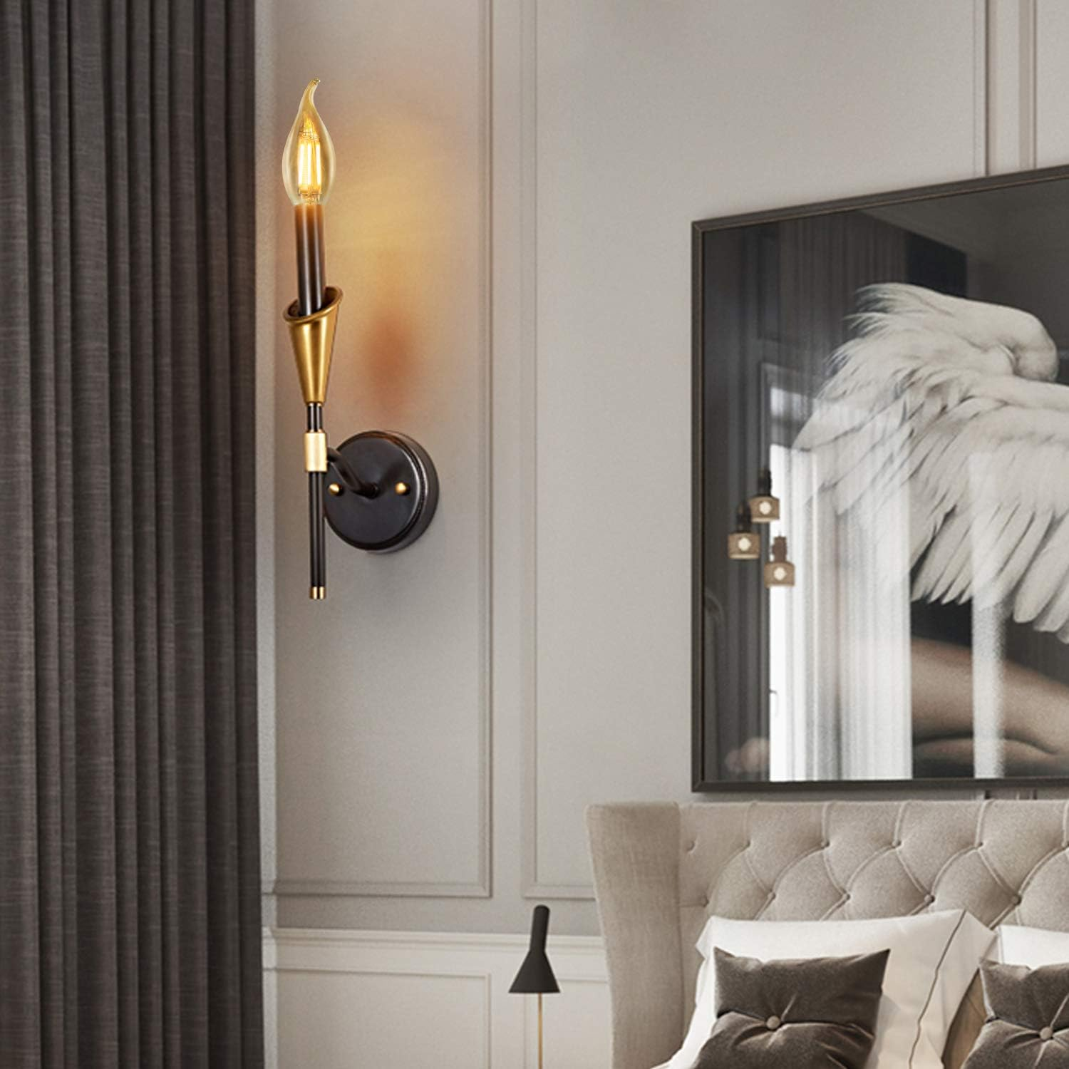 Ein moderner Wandleuchter mit goldener und schwarzer Fassung über einem Bett mit Kunstwerk.