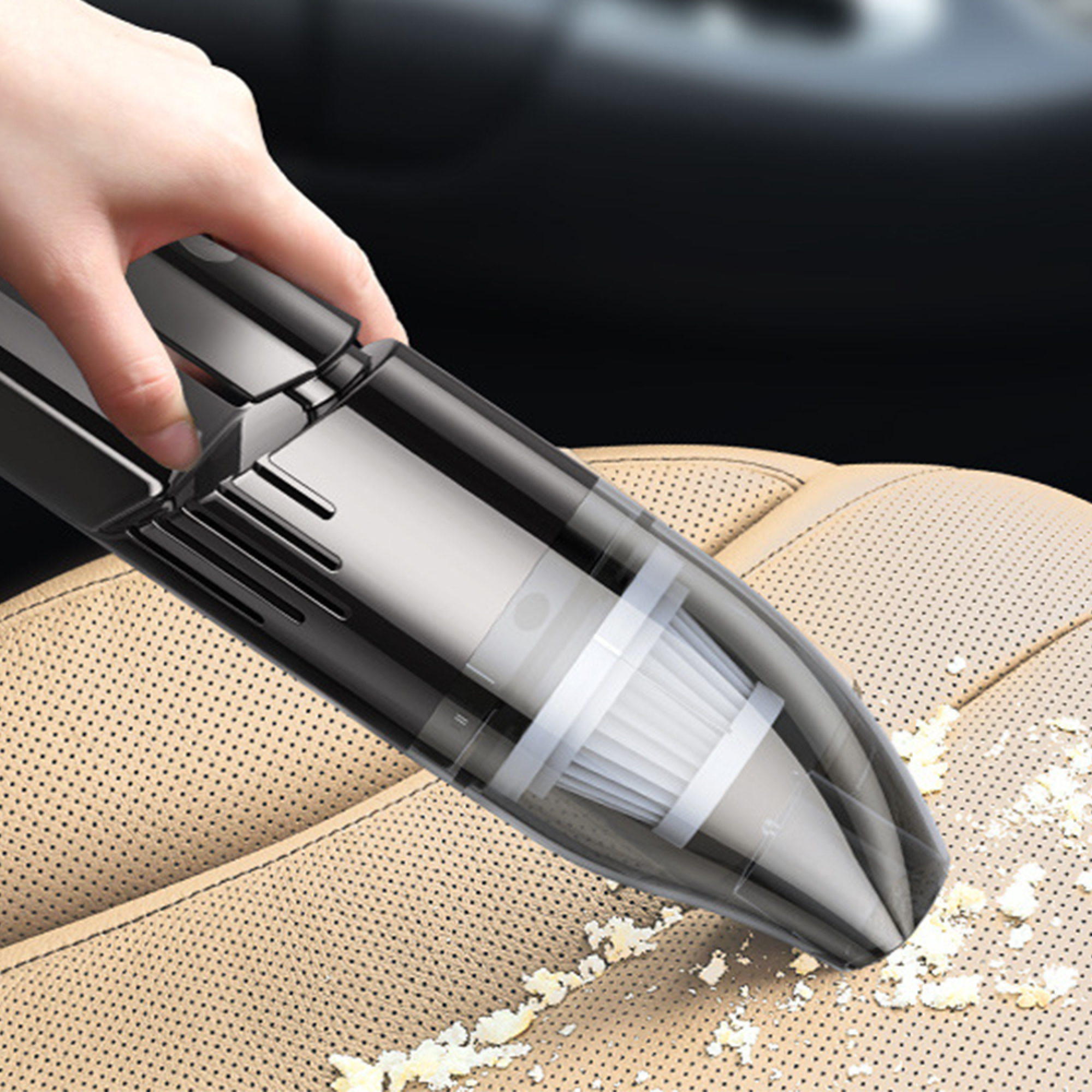 Hand saugt ein Autointerieur mit einem schwarzen Handstaubsauger.
