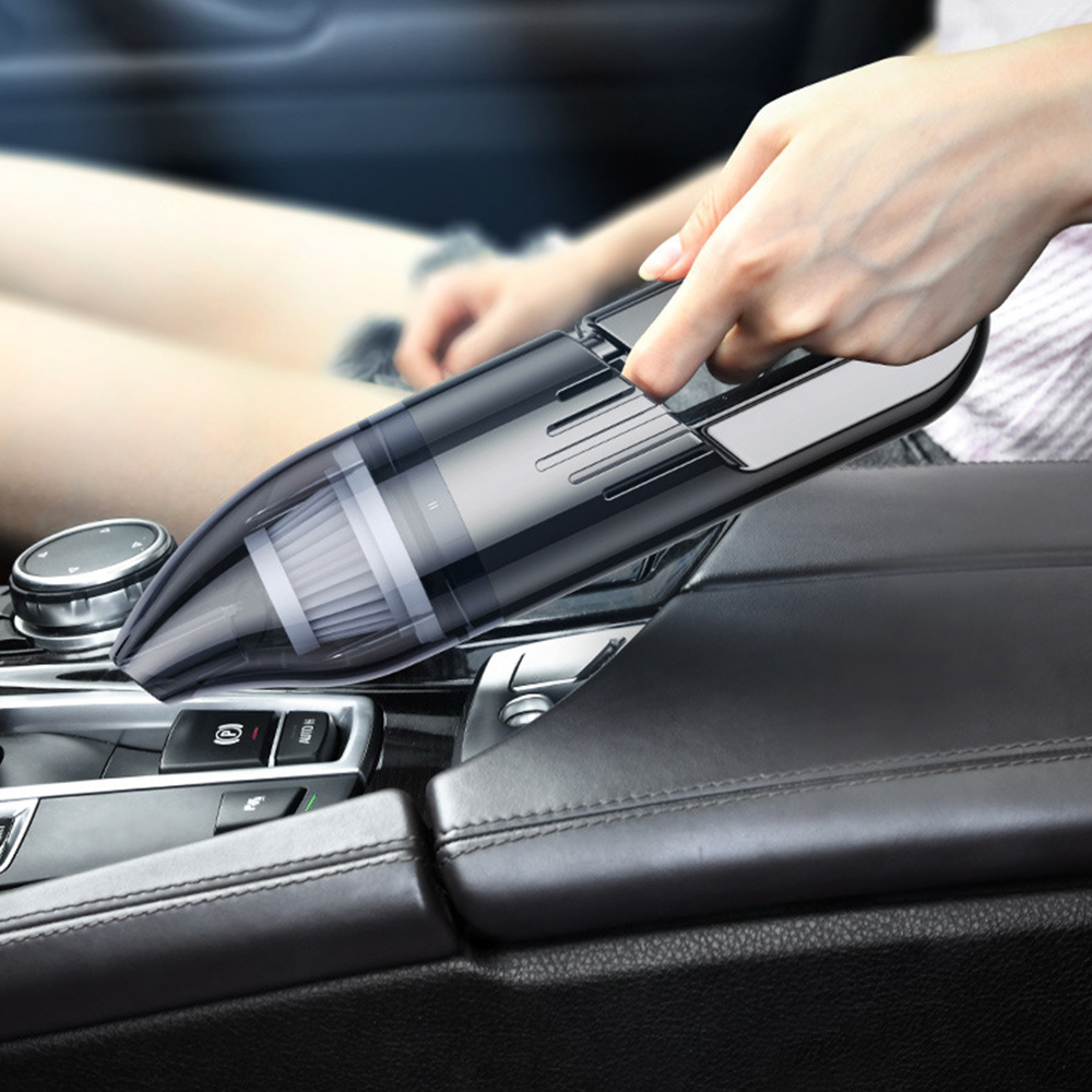 Hand hält schwarzen tragbaren Staubsauger im Auto auf dem Mittelkonsolenbereich.