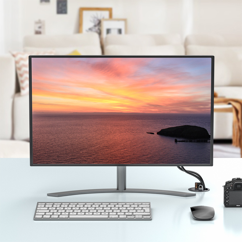 Ein Monitor zeigt einen Sonnenuntergang über dem Meer mit einer kleinen Insel. Tastatur, Maus und Kamera liegen davor.