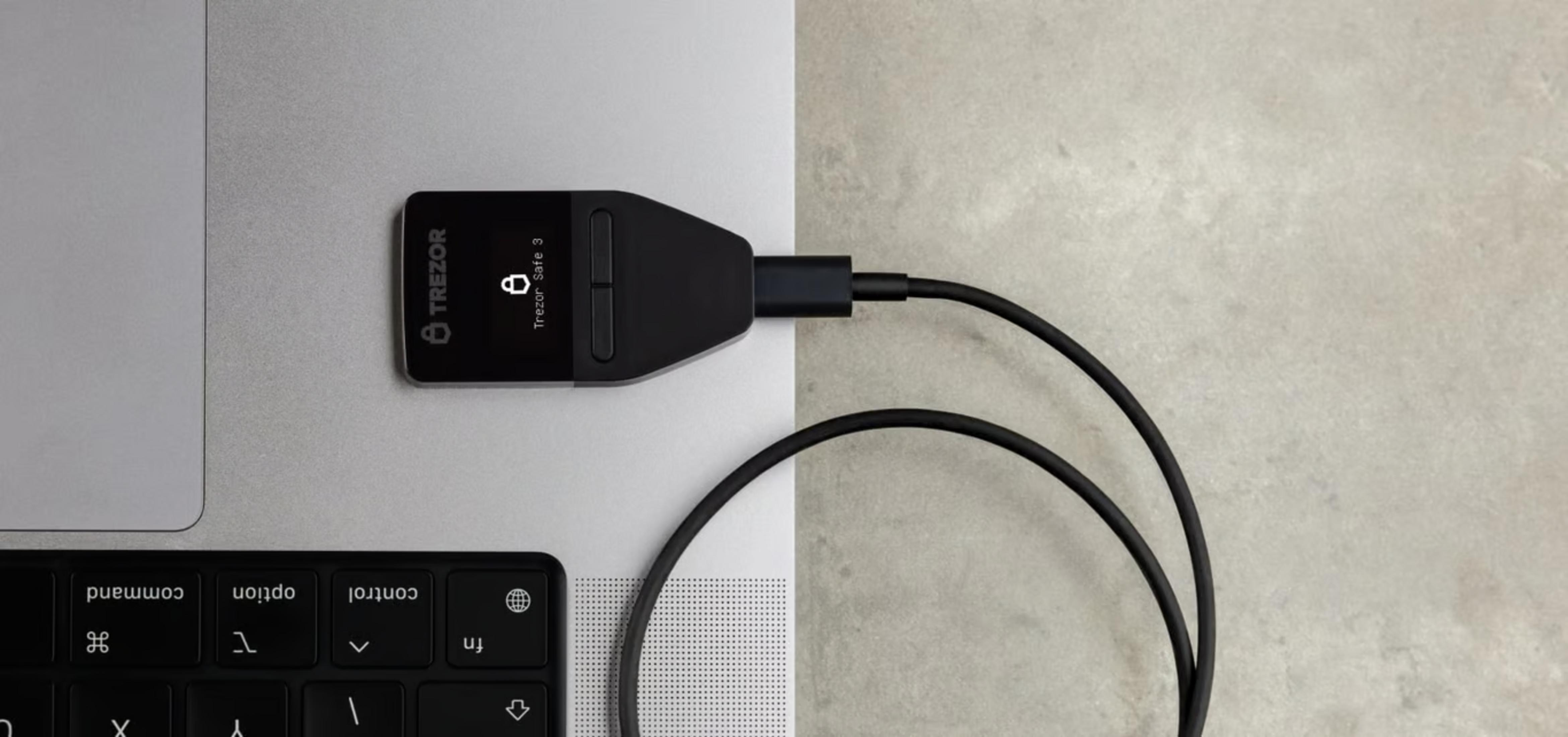 Czarny portfel sprzętowy Trezor Safe 3 jest podłączony przez USB-C do laptopa.