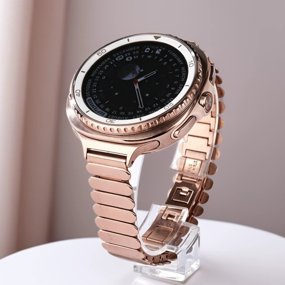 Eine roségoldene Smartwatch mit einem Metallarmband, die auf einem Ständer steht.