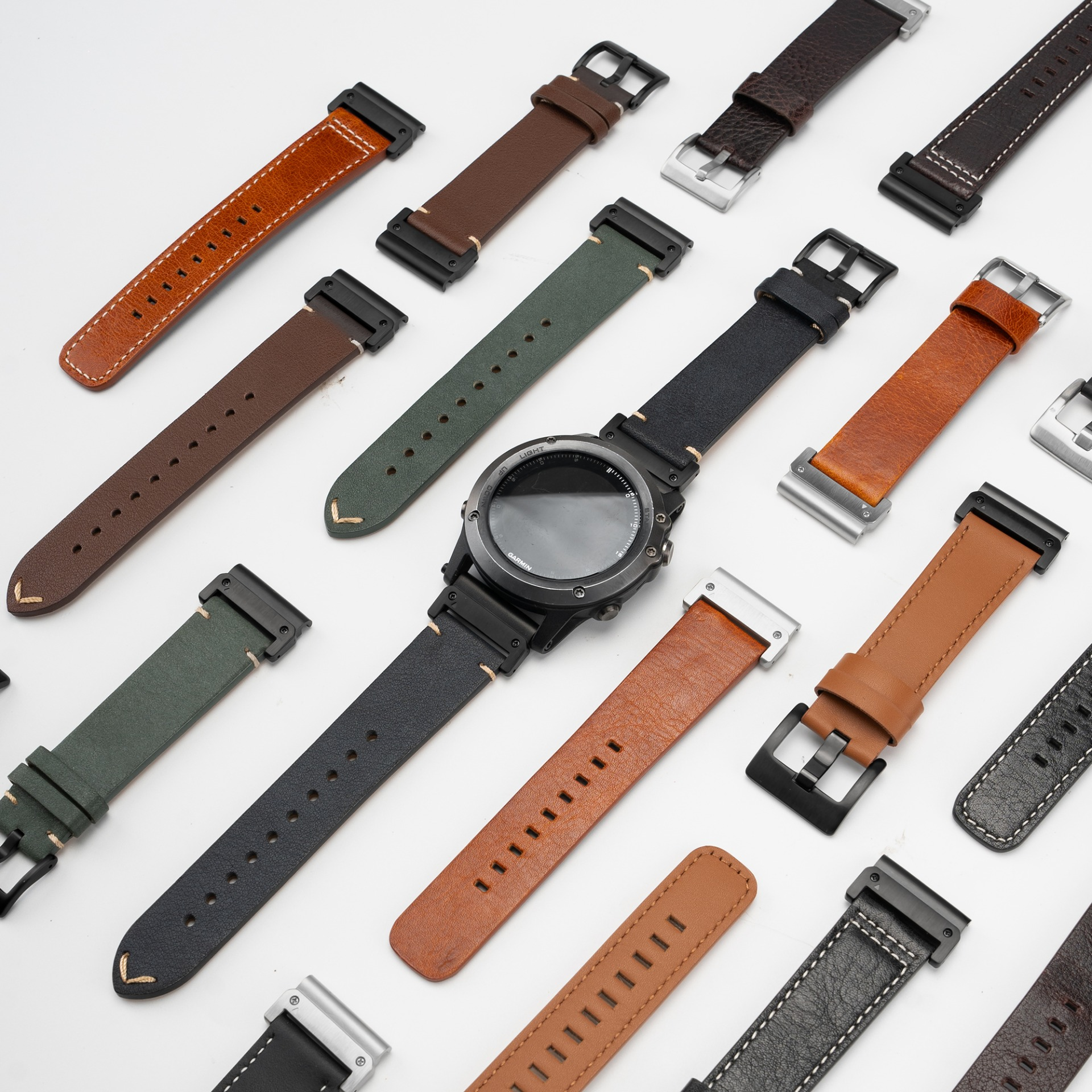 Verschiedene Uhrenarmbänder aus Leder in Braun, Grün und Schwarz, mit einem schwarzen Garmin-Uhrgehäuse.