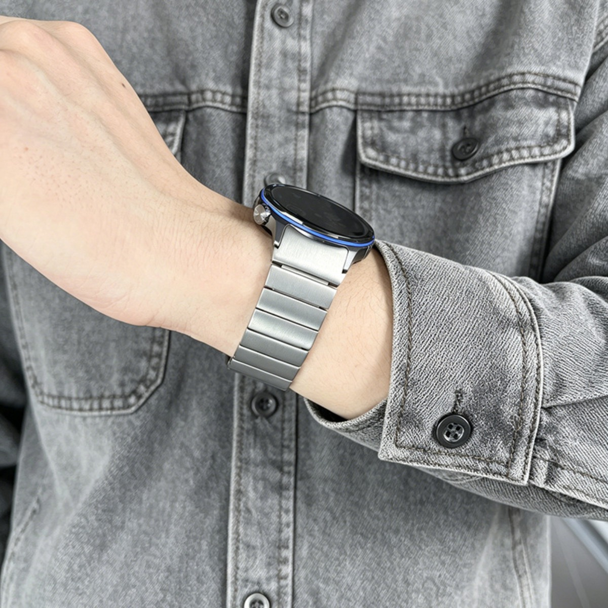 Eine Person trägt eine graue Jeansjacke und eine Smartwatch mit Silikonarmband.