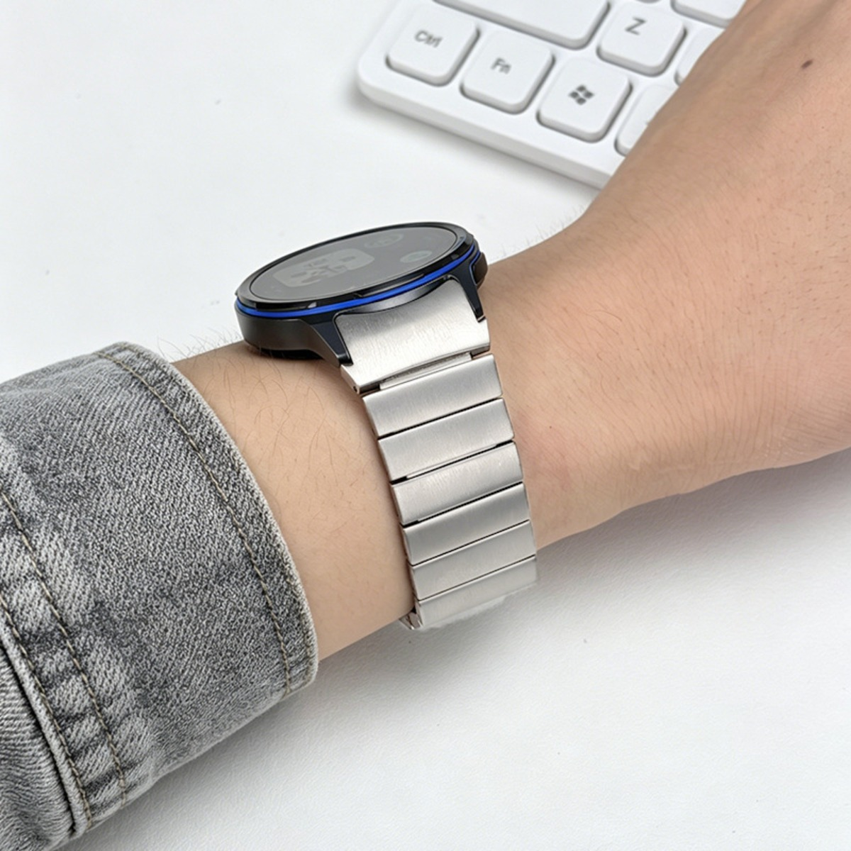 Eine Person trägt eine Smartwatch mit silbernem Armband und blauer Lünette.