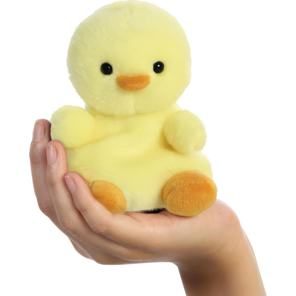 Ein kleines, flauschiges gelbes Entenspielzeug sitzt in einer offenen Handfläche vor weißem Hintergrund.