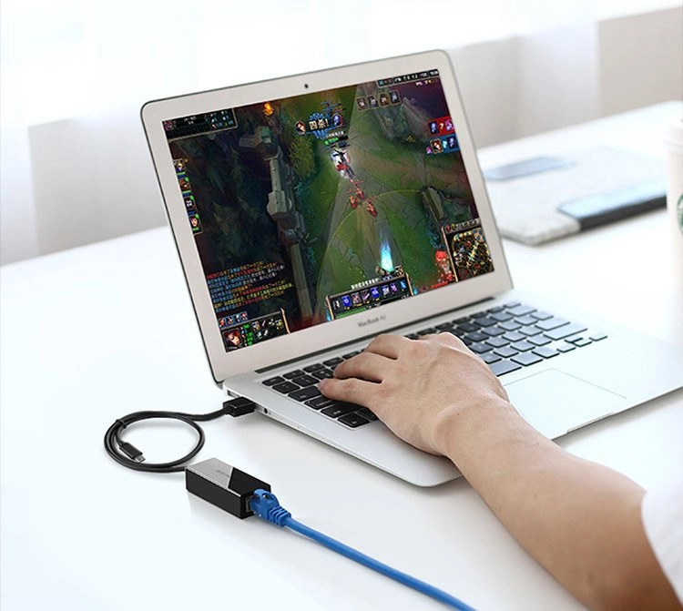 Una persona gioca su un laptop collegato a un adattatore di rete con cavo Ethernet blu.