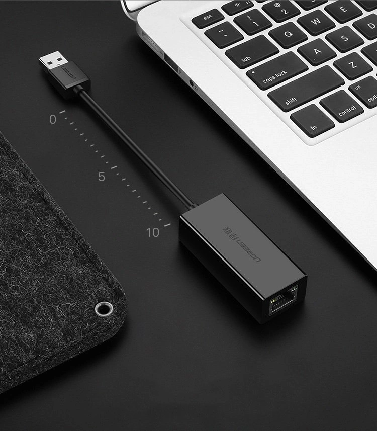 Adattatore USB a Ethernet nero accanto a un laptop e un oggetto in feltro.