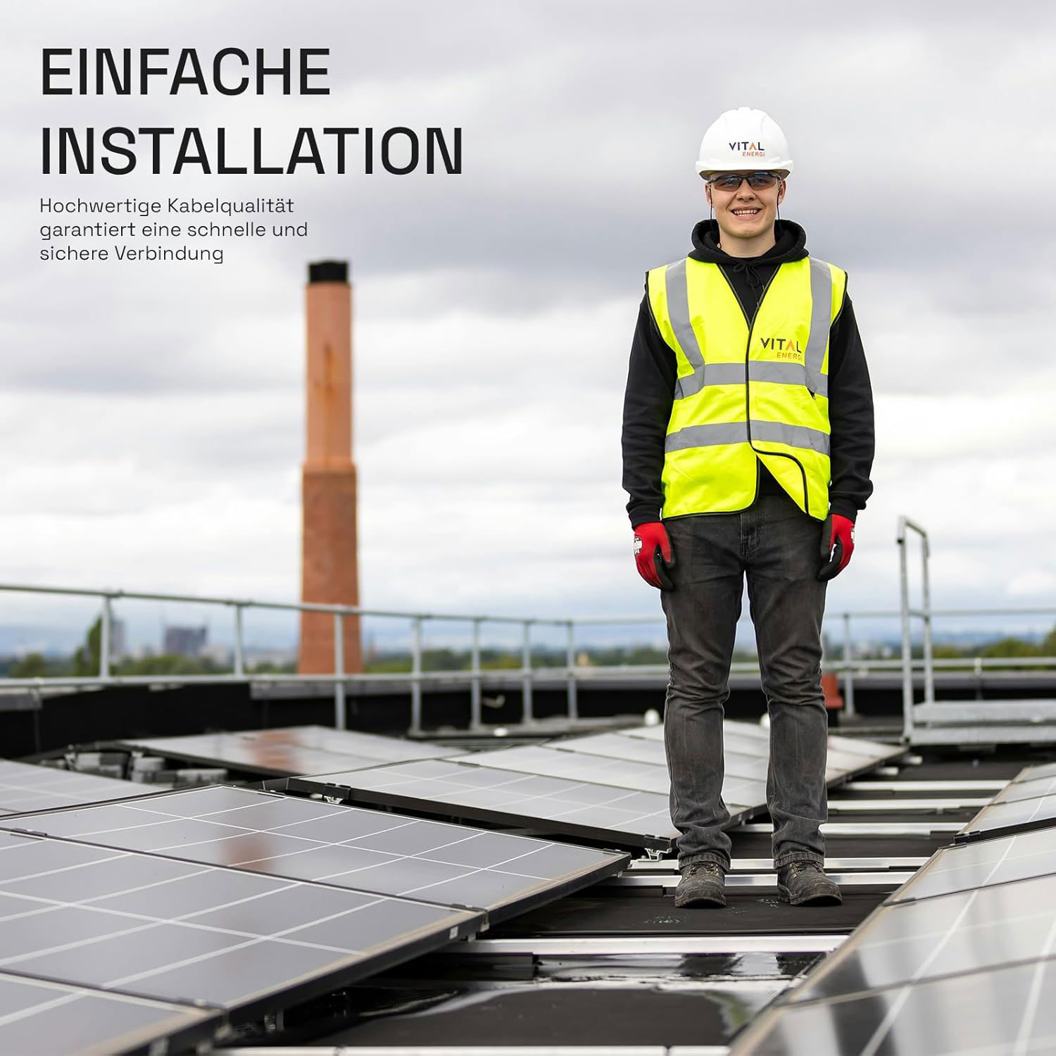 Ein Mann in Warnweste und Helm steht auf einem Dach neben Solarmodulen.