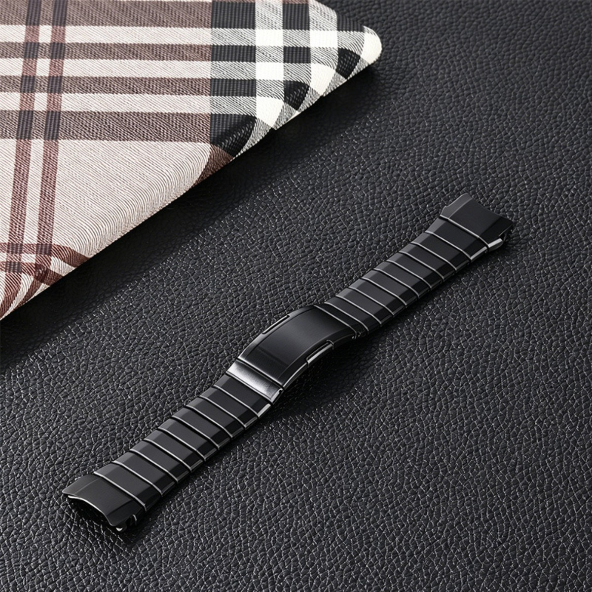 Ein schwarzes Metalluhrenarmband mit kariertem Stoffmuster auf schwarzer Strukturfläche.