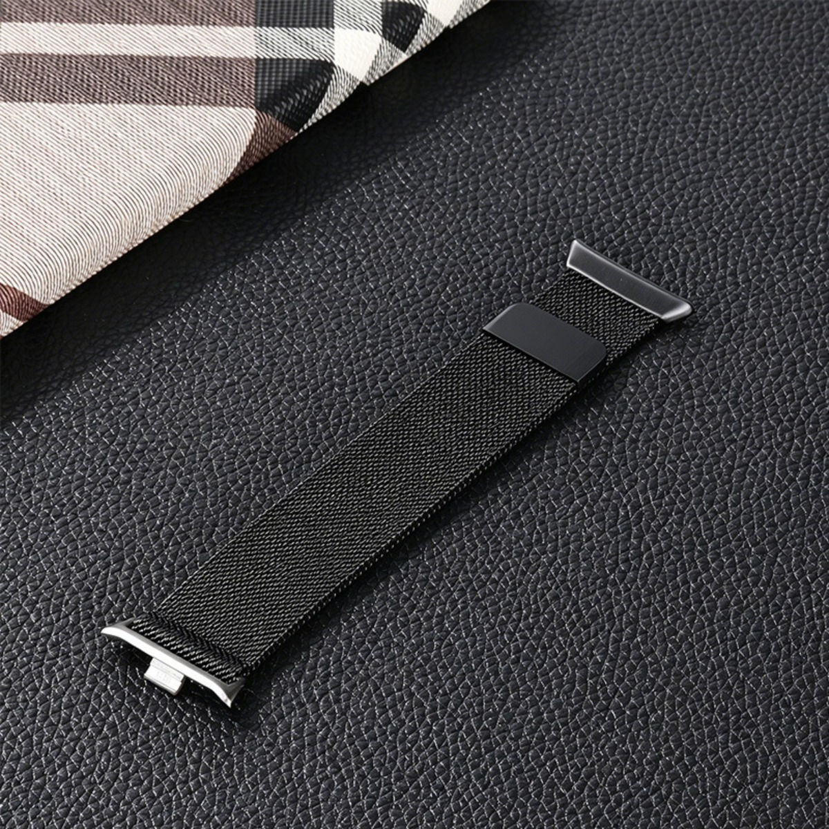 Ein schwarzes, magnetisches Milanese-Uhrenarmband liegt auf einer schwarzen, texturierten Oberfläche.