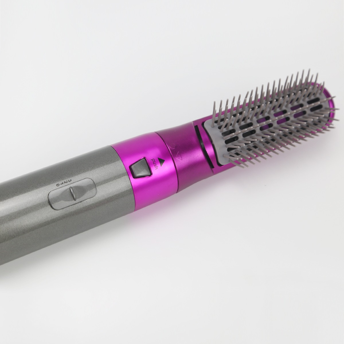 Ein grau-magenta Haarstyling-Tool mit Bürstenaufsatz und Bedienelementen, diagonal auf einer weißen Oberfläche positioniert.