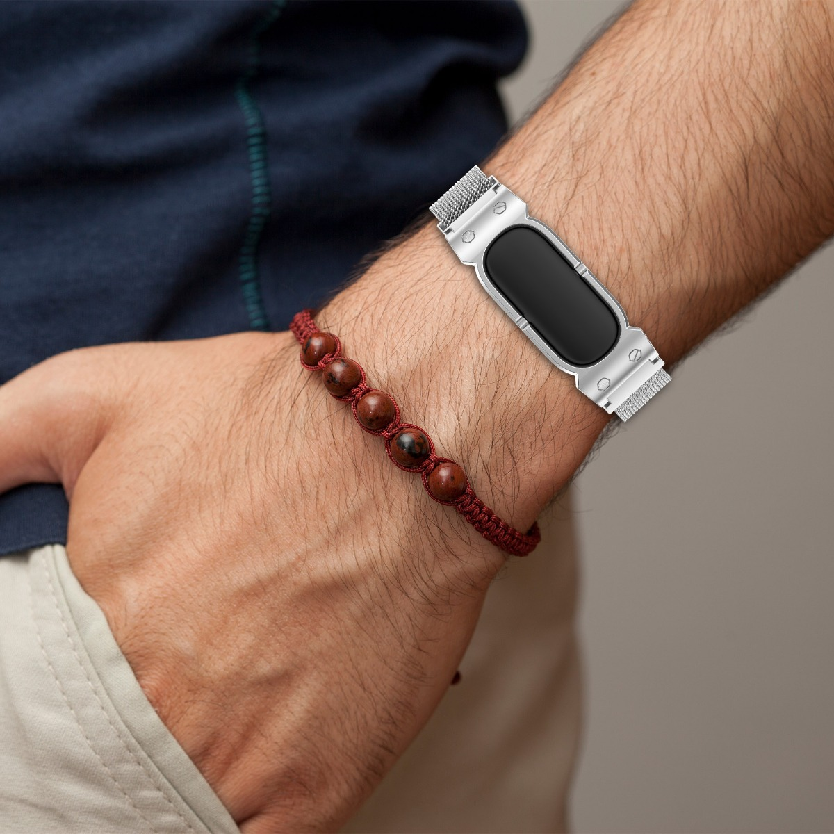 Ein Mann trägt ein silbernes Smartwatch-Armband und ein rotes Perlenarmband.