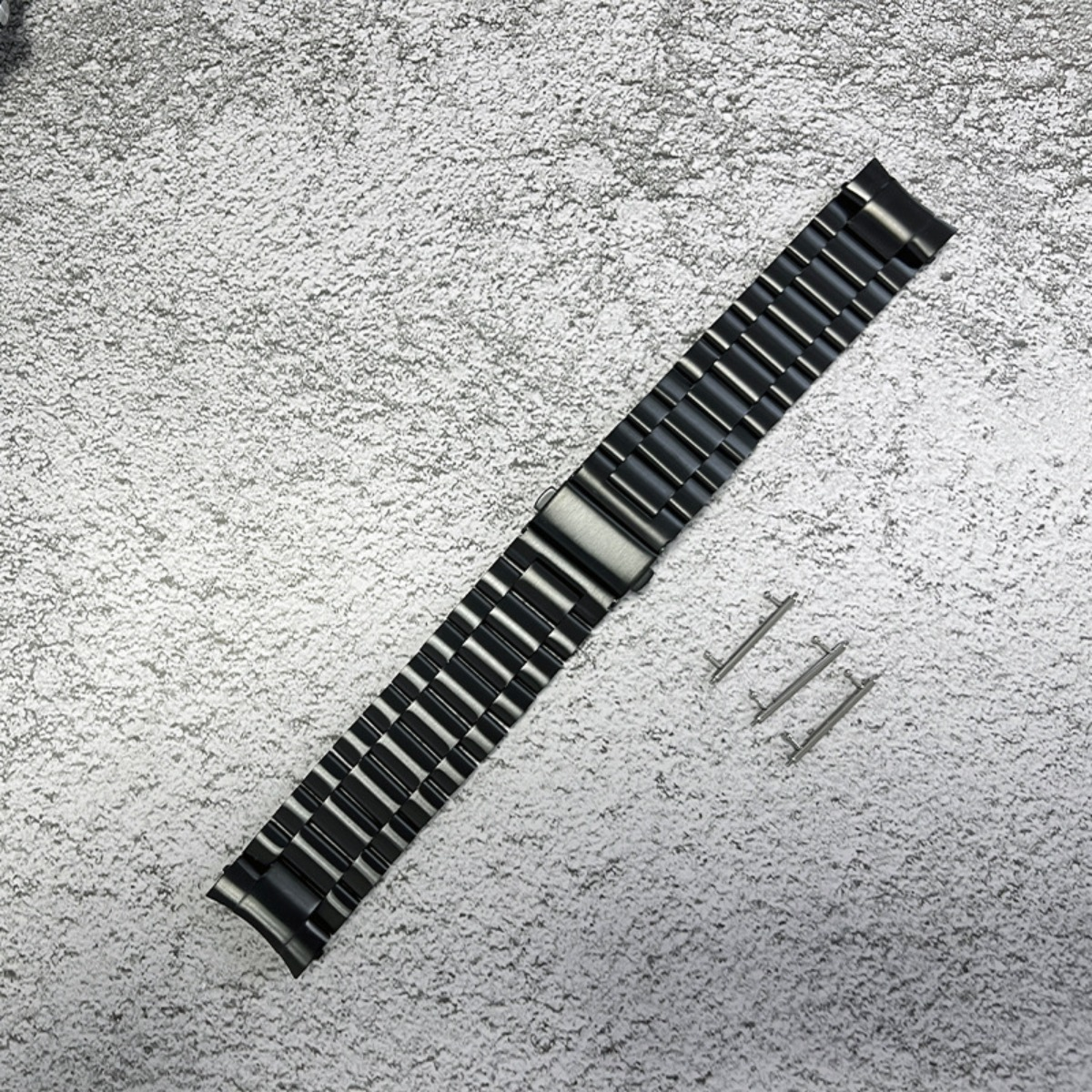 Ein dunkles Metallarmband mit Stiften liegt auf einer strukturierten grauen Oberfläche.
