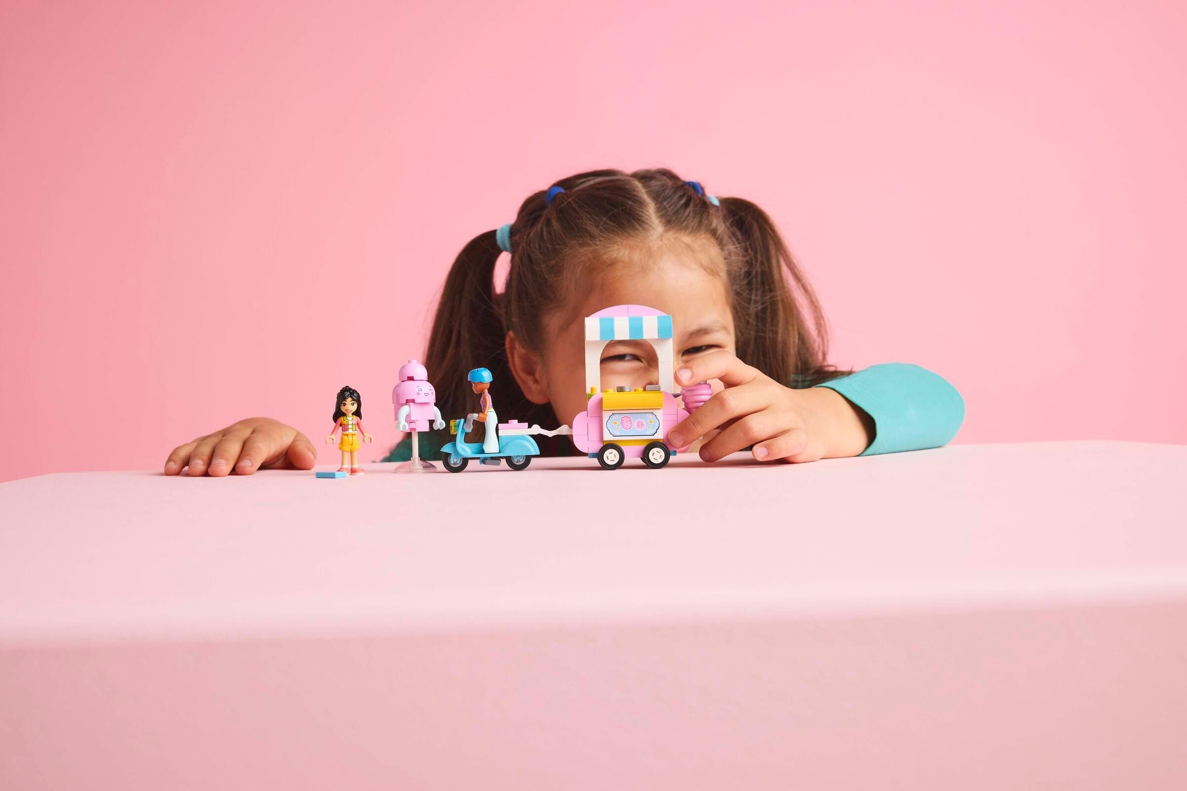 Ein Mädchen mit Pferdeschwänzen spielt mit Lego-Figuren und einem Eiswagen.