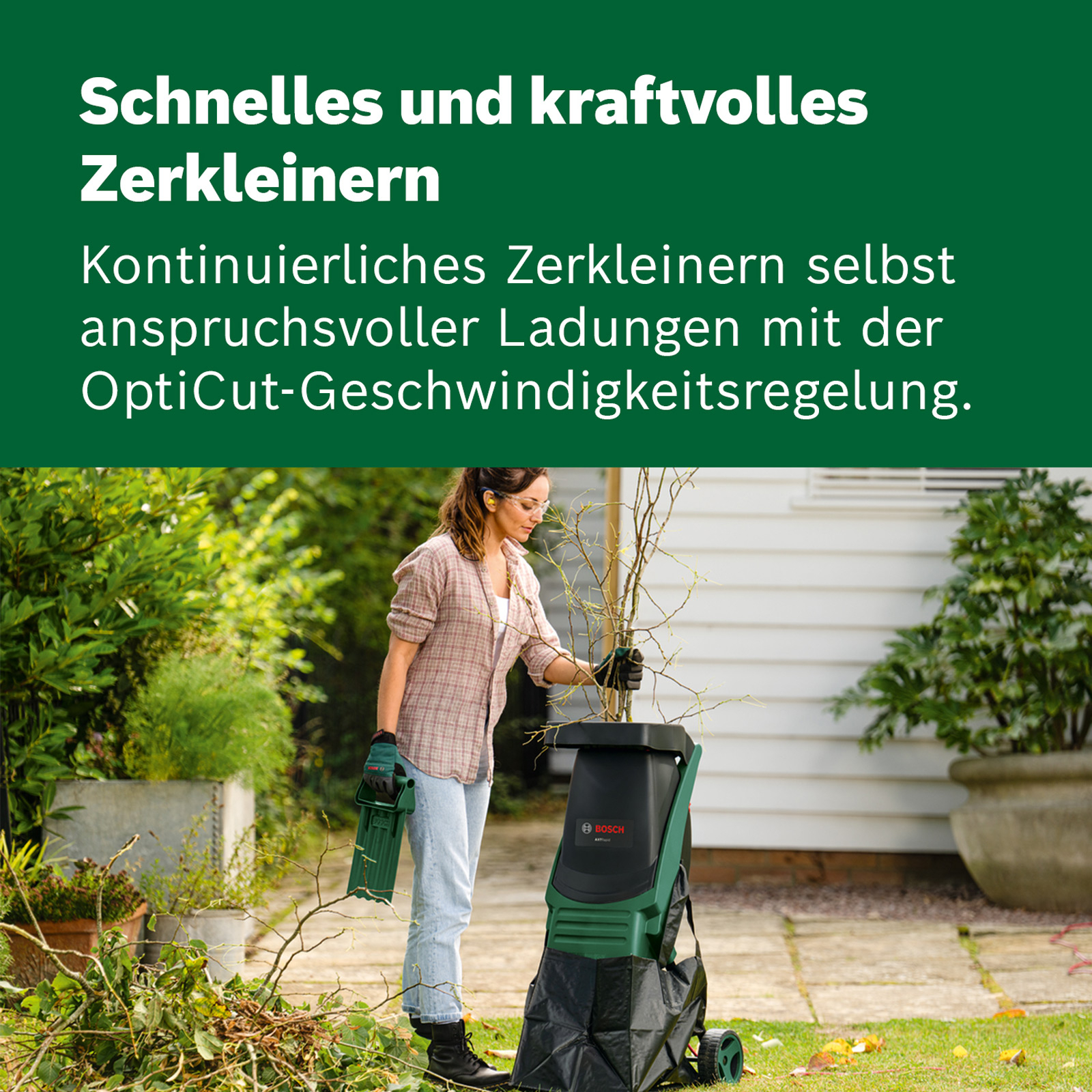 Eine Frau zerkleinert Zweige in einem Bosch-Häcksler im Garten.